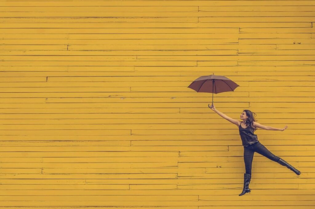 黄色の傘を持って飛び跳ねる女性